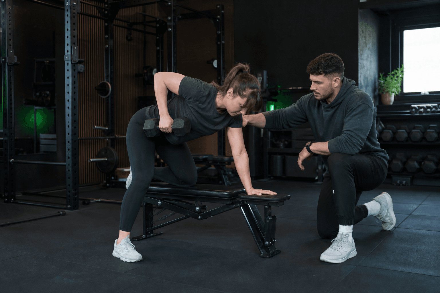 A personal trainer coaching a member through a dumbbell row in a private gym